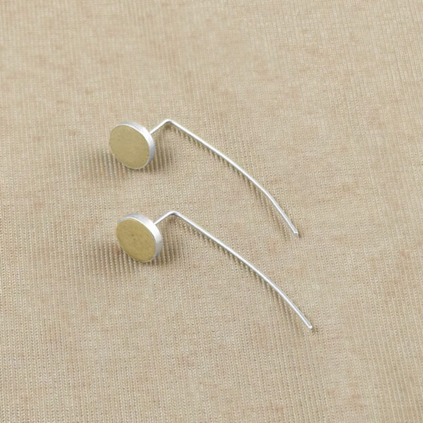 Flat lay of two Golden Kiss Geometric Earrings showing the round clay disc and curved sterling silver wire against a natural linen textile.