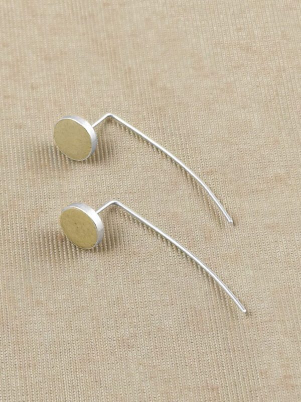 Flat lay of two Golden Kiss Geometric Earrings showing the round clay disc and curved sterling silver wire against a natural linen textile.