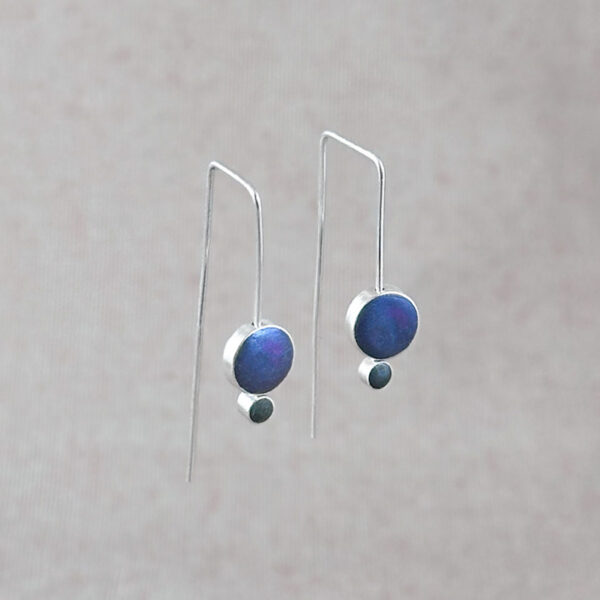 Sterling silver Orbit Drop Earrings with iridescent peacock blue and gray hand-tinted clay circles, angled product shot on neutral background.
