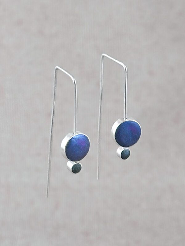 Sterling silver Orbit Drop Earrings with iridescent peacock blue and gray hand-tinted clay circles, angled product shot on neutral background.