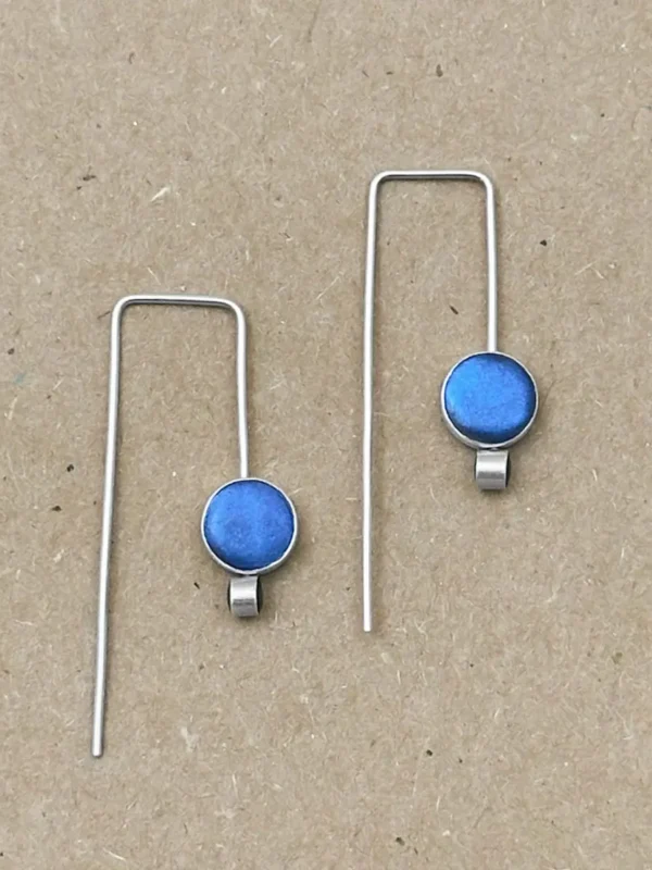 Flat lay of Orbit Drop Earrings in sterling silver with peacock blue hand-tinted clay circles on natural linen background.