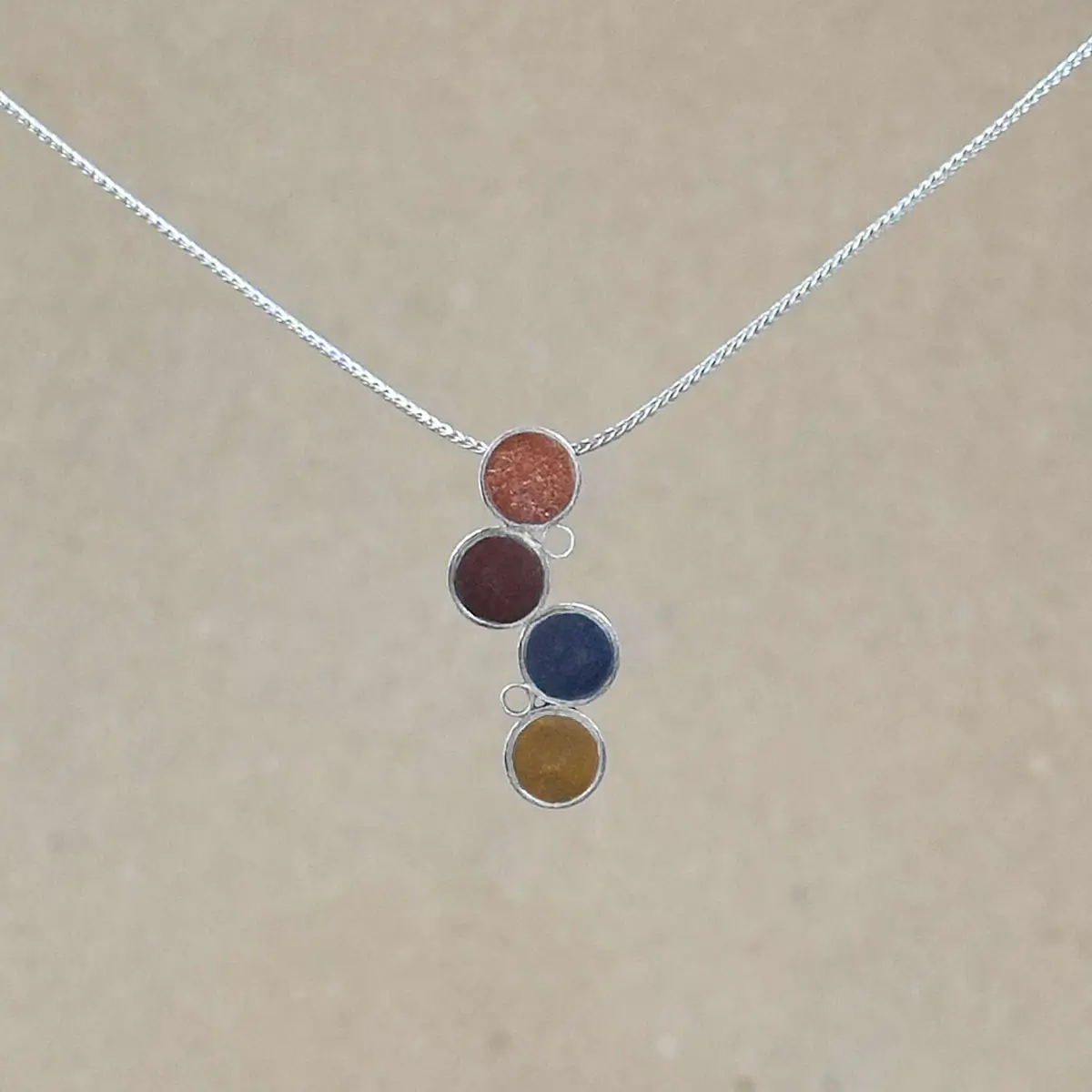 Sterling silver Cascade Pendant with four offset circles of metallic hand-tinted clay in terracotta, burgundy, slate gray, and ochre, on an adjustable silver foxtail chain.