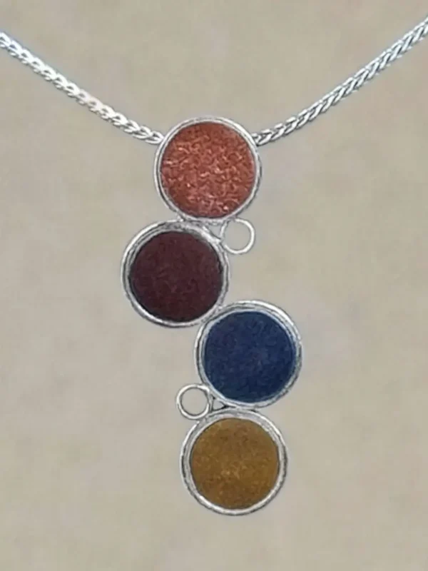 Close-up of the Cascade Pendant showing the metallic sheen and fine glitter texture of four hand-tinted clay discs in terracotta, burgundy, slate gray, and ochre, set in sterling silver circles.