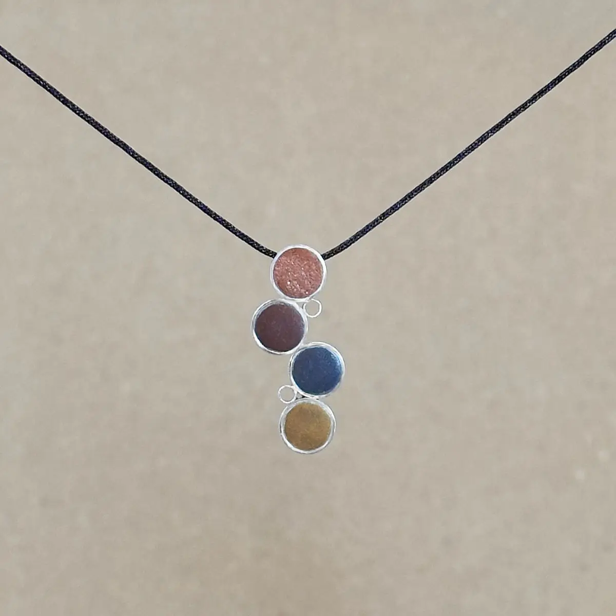 N-GBW_geometric-bubbles-pendant-warm_cord_resized The Cascade Pendant on an adjustable brown kumihimo cord, showing the full drop of four offset sterling silver circles with warm-toned metallic clay.
