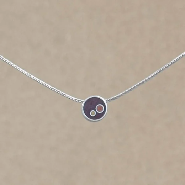 A small sterling silver circle pendant on a silver foxtail chain, centered against a warm beige background. The pendant holds deep brownish-copper hand-tinted clay inset with two smaller circles in gold and copper tint.
