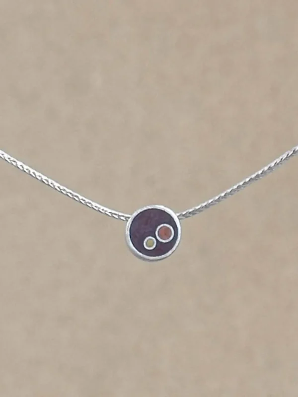 A small sterling silver circle pendant on a silver foxtail chain, centered against a warm beige background. The pendant holds deep brownish-copper hand-tinted clay inset with two smaller circles in gold and copper tint.