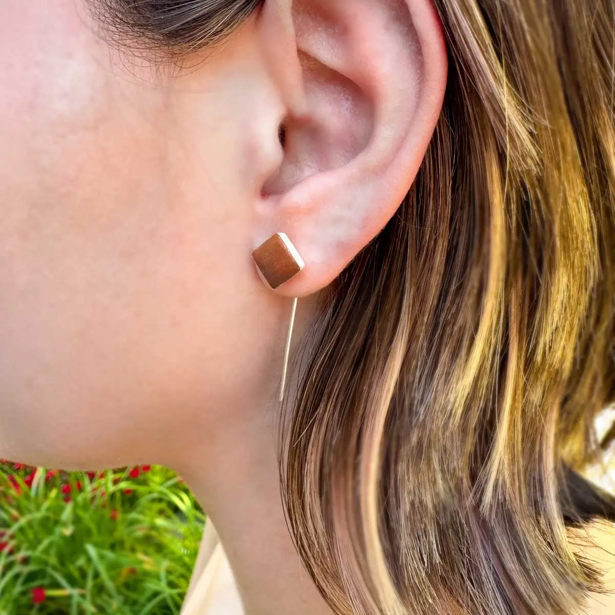 Woman wearing copper diamond stud earring with long thin silver wire dangle