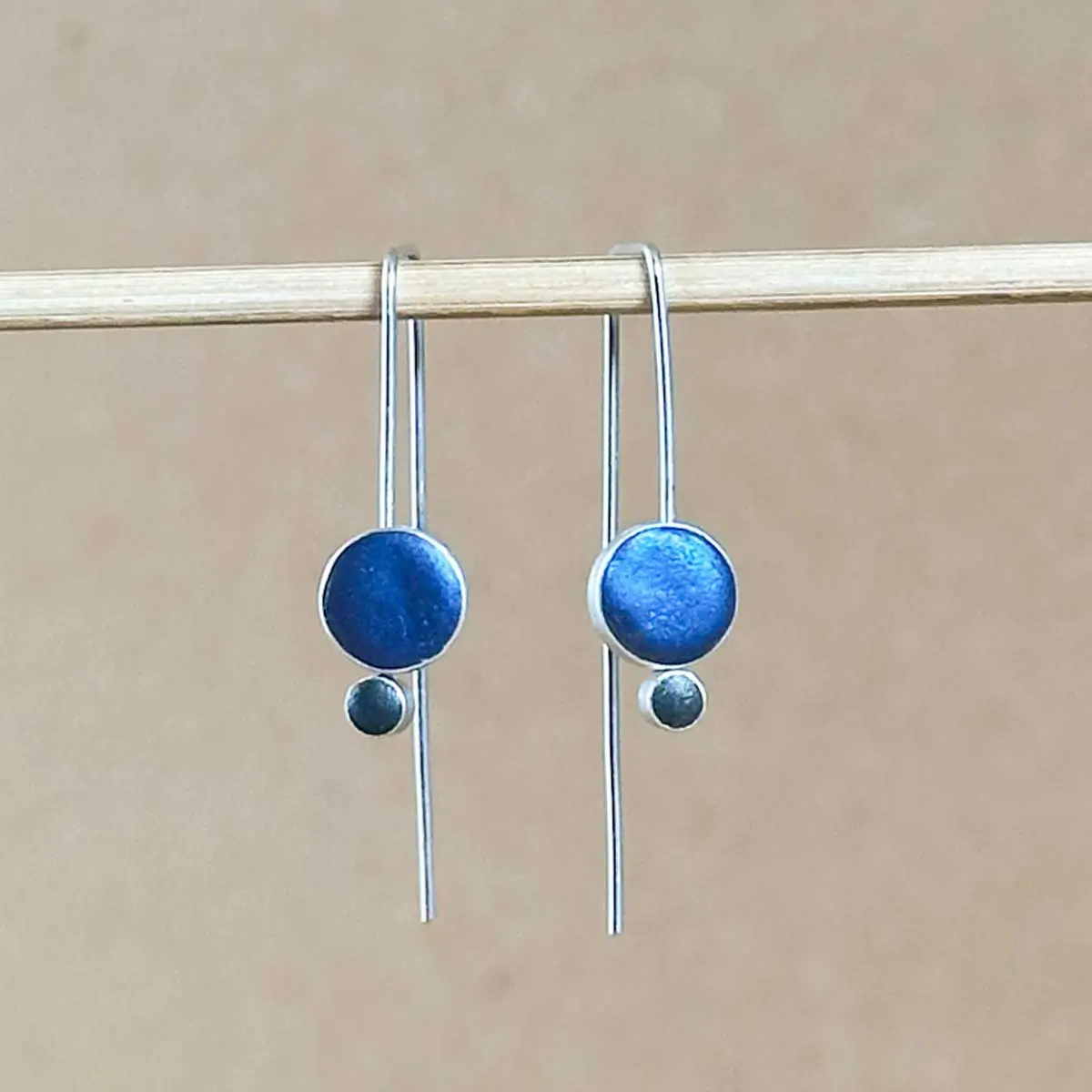 Front view of sterling silver Orbit Drop Earrings showing two-circle drop detail in peacock blue and dark gray hand-tinted clay.