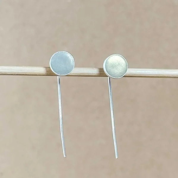 Sterling silver drop earrings with round champagne gold clay discs, floating against a warm taupe background.